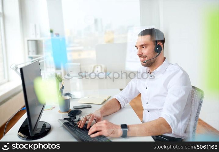 business, people, communication and technology concept - smiling businessman or helpline operator with headset and computer typing at office. businessman with headset and computer at office