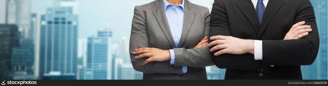 business, people, cooperation and education concept - close up of businesswoman and businessman with crossed arms over city background