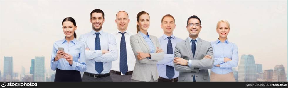 business, people, corporate, teamwork and office concept - group of happy businesspeople with crossed arms over city background