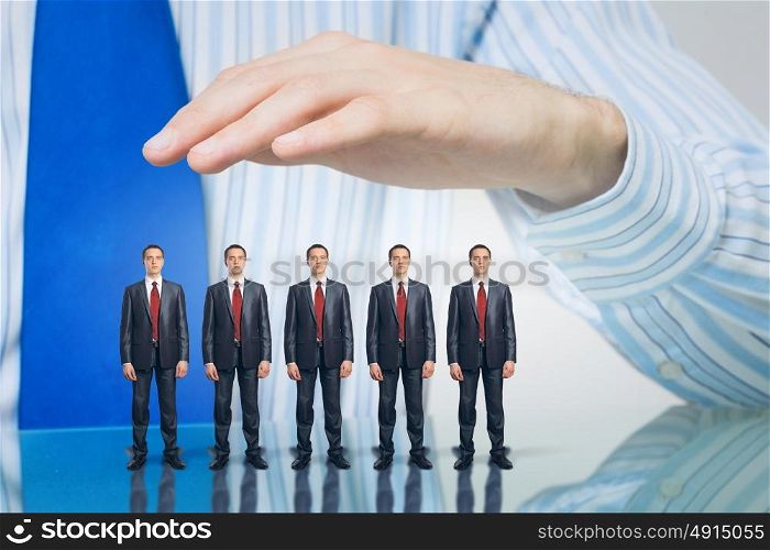 Business people covered with palm. Male hand protecting business people of different size