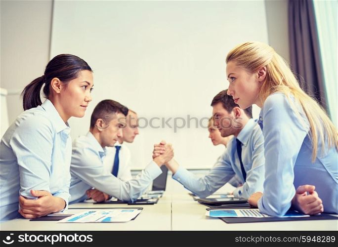 business, people, crisis and confrontation concept - smiling business team sitting on opposite sides and arm wrestling in office