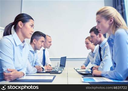 business, people, crisis and confrontation concept - smiling business team sitting on opposite sides in office. smiling business people having conflict in office
