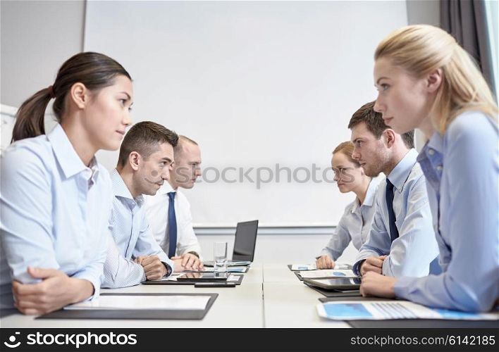 business, people, crisis and confrontation concept - smiling business team sitting on opposite sides in office