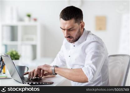 business, people, deadline, time and technology concept - stressed businessman with laptop computer looking at his wristwatch at office. businessman with laptop and wristwatch at office