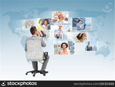 business, people, design and choice concept - businessman sitting in office chair and looking at different images over blue background from back