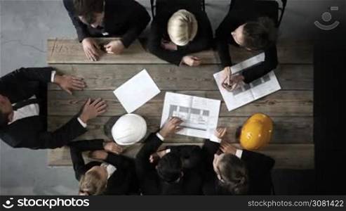 Business people discuss construction blueprint, hardhat on office table