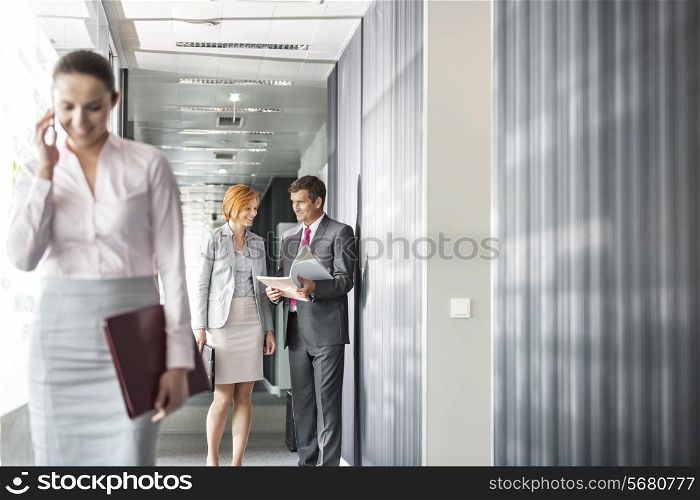 Business people discussing in corridor with colleague using cell phone in foreground