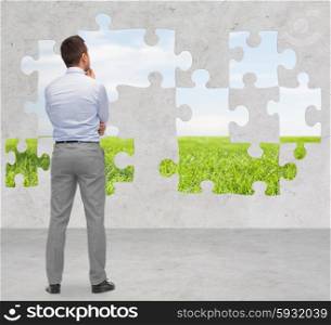 business, people, ecology and strategy concept - businessman thinking from back over puzzle with natural landscape and concrete room background