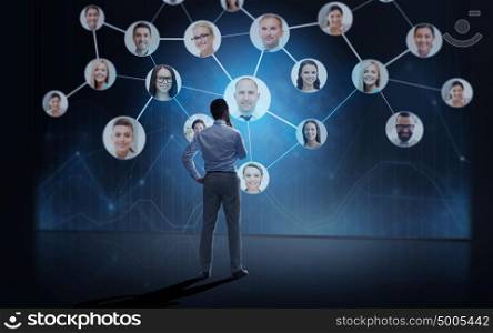 business, people, employment, headhunting and network concept - businessman looking at virtual contact projection over dark background from back. businessman looking at over dark