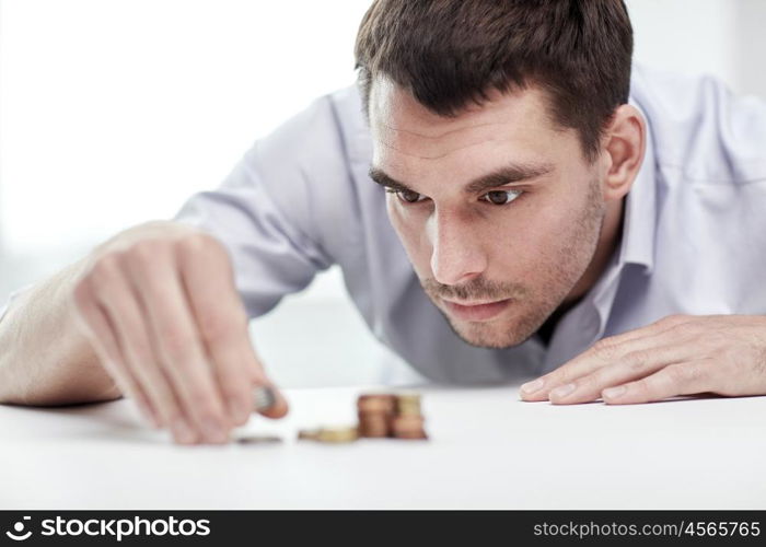 business, people, finances and money saving concept - businessman putting coins into piles at office