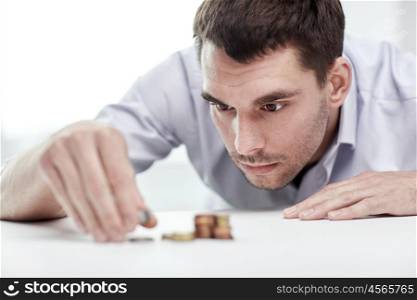 business, people, finances and money saving concept - businessman putting coins into piles at office