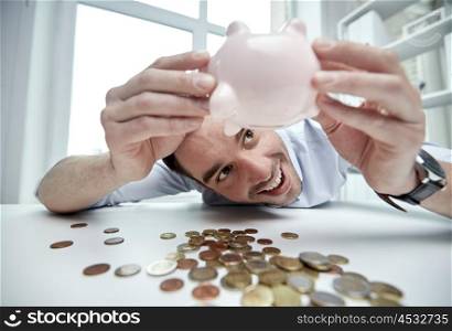 business, people, finances and money saving concept - happy businessman shaking piggy bank and getting coins at office