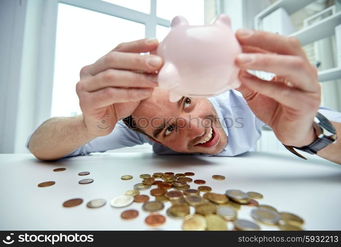 business, people, finances and money saving concept - happy businessman shaking piggy bank and getting coins at office