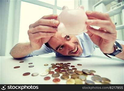 business, people, finances and money saving concept - happy businessman shaking piggy bank and getting coins at office