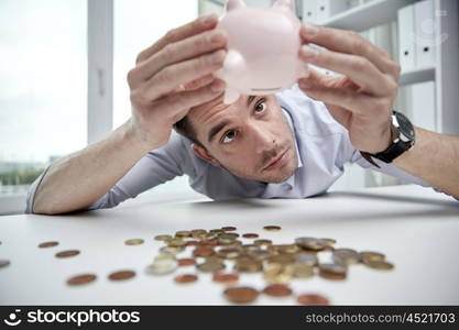 business, people, finances, crisis and money saving concept - businessman shaking piggy bank and getting coins at office