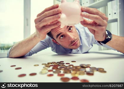 business, people, finances, crisis and money saving concept - businessman shaking piggy bank and getting coins at office