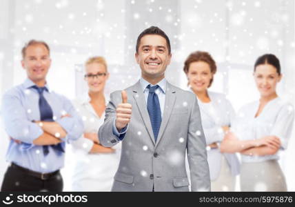 business, people, gesture and office concept - happy businessman with team showing thumbs up over office background and snow effect