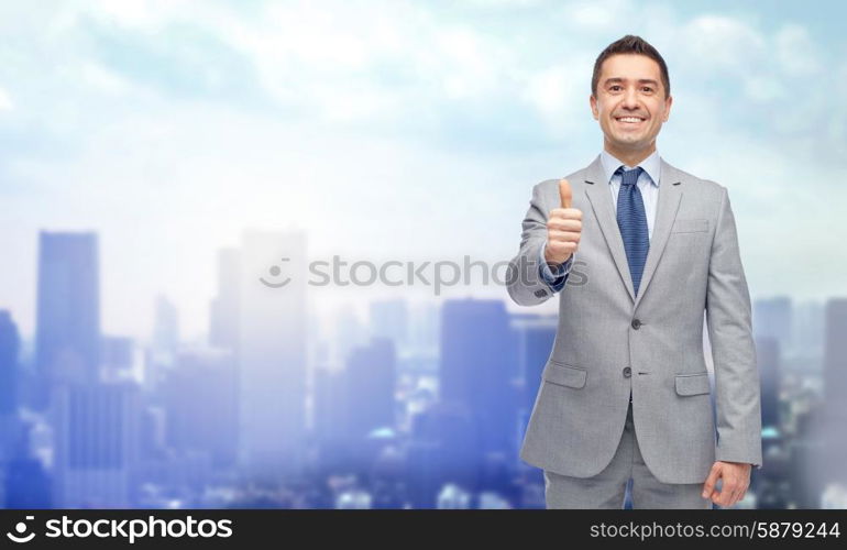 business, people, gesture and success concept - happy smiling businessman in suit showing thumbs up over city background