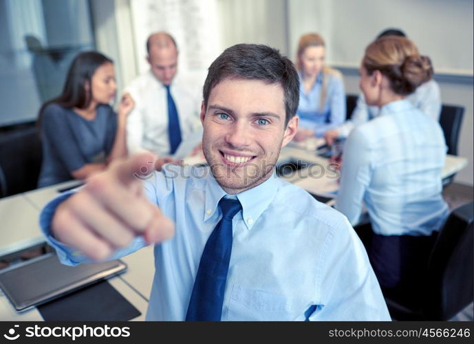 business, people, gesture and teamwork concept - smiling businessman pointing finger to you with group of businesspeople meeting in office