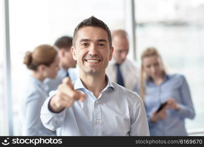 business, people, gesture and teamwork concept - smiling businessman pointing finger to you with group of businesspeople meeting in office