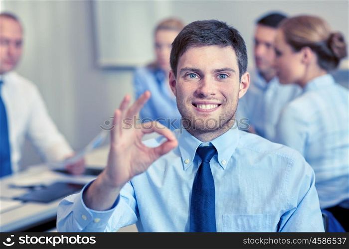 business, people, gesture and teamwork concept - smiling businessman showing ok gesture with group of businesspeople meeting in office