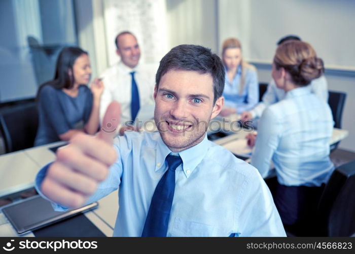 business, people, gesture and teamwork concept - smiling businessman showing thumbs up with group of businesspeople meeting in office