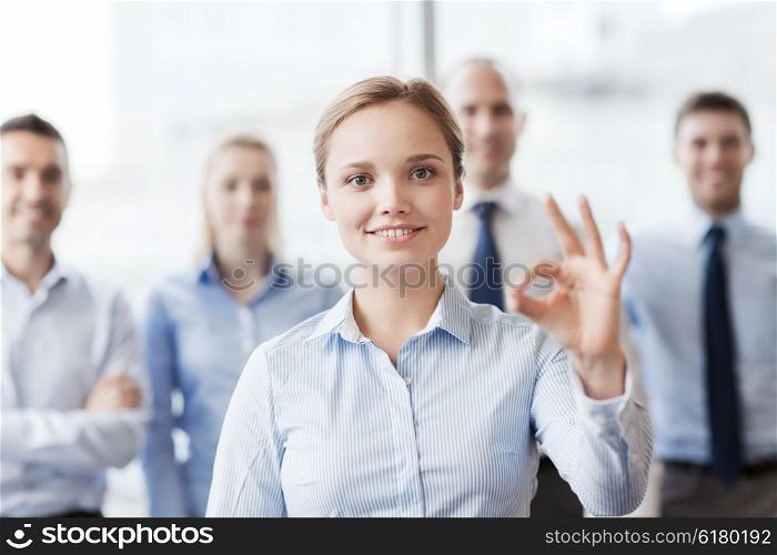 business, people, gesture and teamwork concept - smiling businesswoman showing ok sign with group of businesspeople in office