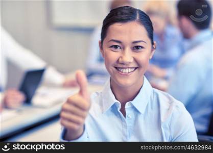 business, people, gesture and teamwork concept - smiling businesswoman showing thumbs up with group of businesspeople meeting in office. group of smiling businesspeople meeting in office