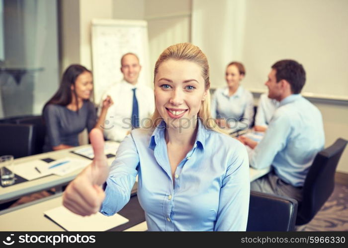 business, people, gesture and teamwork concept - smiling businesswoman showing thumbs up with group of businesspeople meeting in office