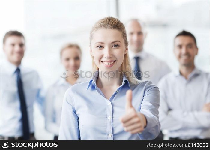 business, people, gesture and teamwork concept - smiling businesswoman showing thumbs up with group of businesspeople in office