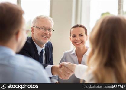 business, people, gesture, cooperation and partnership concept - smiling senior businessman making handshake with woman at office