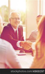 business, people, gesture, cooperation and partnership concept - smiling senior businessman making handshake with woman at office. senior businessman making handshake at office