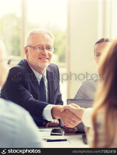 business, people, gesture, cooperation and partnership concept - smiling senior businessman making handshake with woman at office. senior businessman making handshake at office