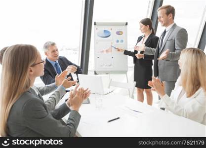 Business people giving presentation using financial diagrams at flipchart to colleagues in office at meeting. Business people giving presentation