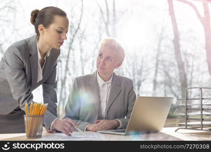 Business people having a team meeting. Warsaw, Poland.. Confident mature businesswoman looking at colleague explaining document at desk against window in office
