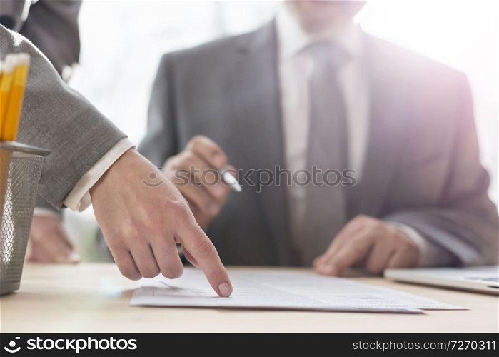 Business people having a team meeting. Warsaw, Poland.. Hand of businesswoman pointing at document to senior businessman in office
