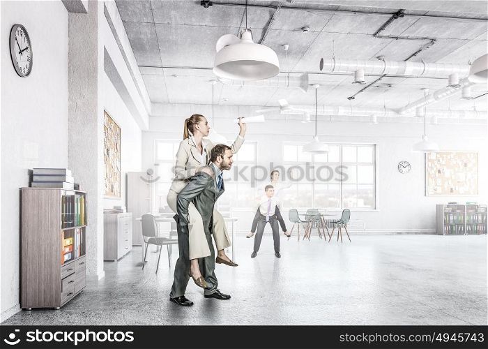 Business people having break in office. Businesswoman riding on back of her colleague in modern office