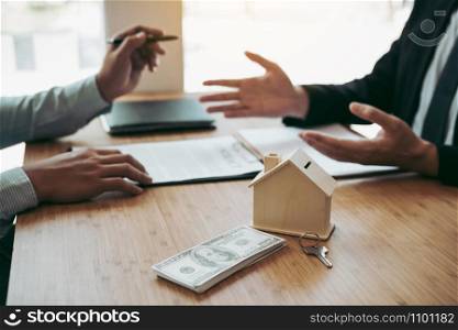 Business people home sales broker is using a pen pointing to the house model and describing the various components of the house.