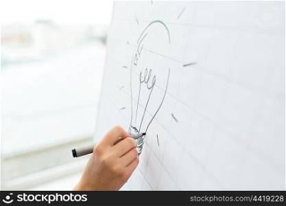 business, people, idea, startup and education concept - close up of hand with marker drawing light bulb on flip chart at office