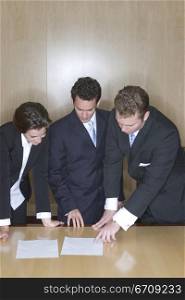 Business People in a board room pointing at a document on the table looking down