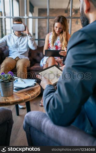 Business people in an informal work meeting using tablet and virtual reality glasses. Selective focus on tablet in foreground.. Business people using tablet and virtual reality glasses