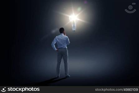 business, people, inspiration and idea concept - businessman looking at lighting bulb over dark background from back. businessman looking at lighting bulb over dark