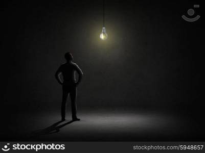 business, people, inspiration and idea concept - businessman looking at lighting bulb in dark room from back