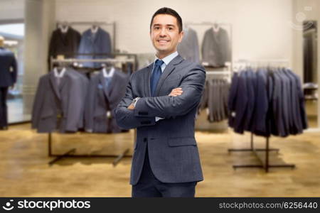 business, people, menswear, sale and clothes concept - happy smiling businessman in suit over clothing store background