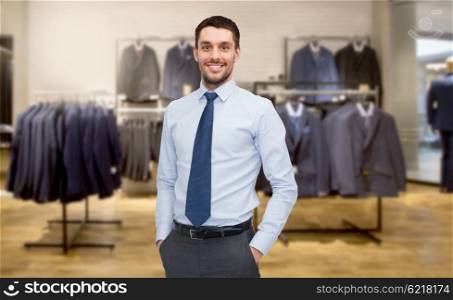 business, people, menswear, sale and clothes concept - happy young businessman over clothing store background