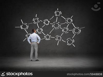 business, people, network and communication concept - businessman looking at network scheme over concrete room background from back