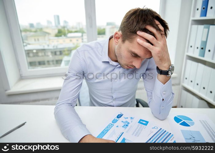 business, people, paperwork and deadline concept - stressed businessman with papers and charts sitting at table in office