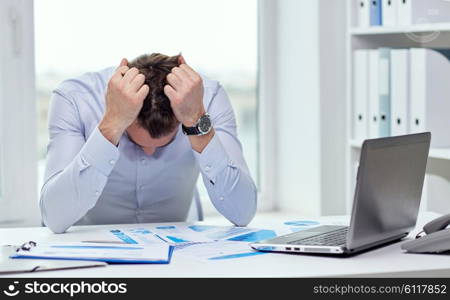 business, people, paperwork and deadline concept - stressed businessman with papers and charts sitting at table in office