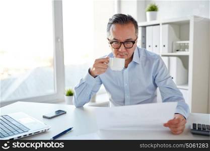 business, people, paperwork and technology concept - businessman reading paper and drinking coffee at office. businessman with papers drinking coffee at office