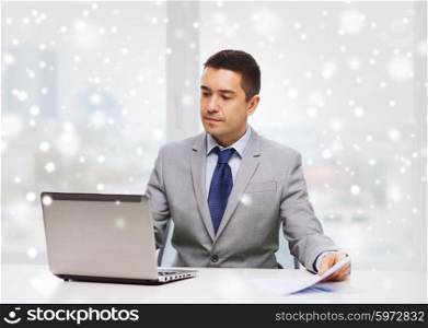 business, people, paperwork and technology concept - businessman with laptop computer and papers working in office over snow effect
